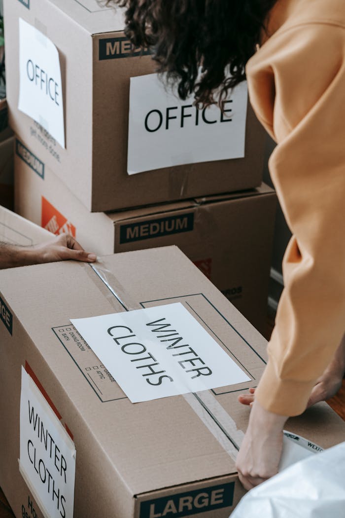 about-img Close-up of people packing labeled boxes for moving day at home.